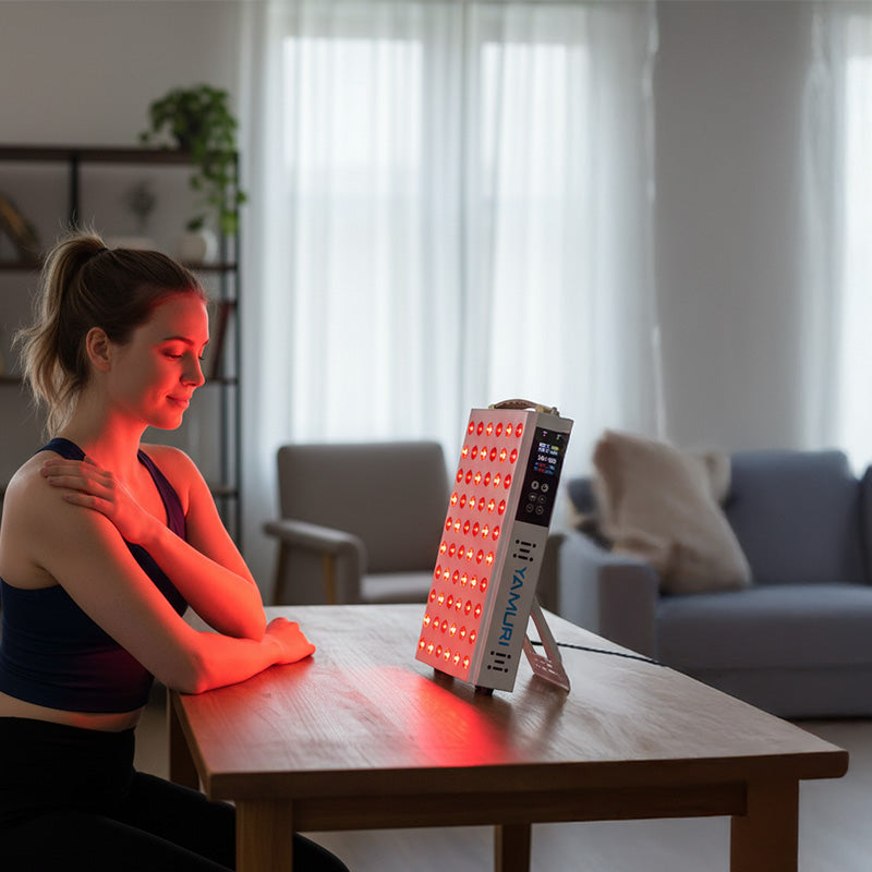 Woman in yoga outfit using red light therapy panel in living room for daily wellness