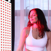 Woman relaxing under red light therapy panel for skin and muscle recovery at home