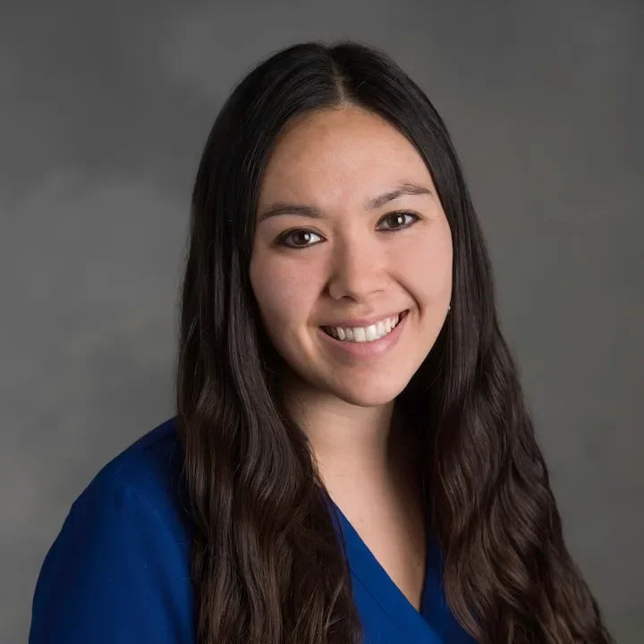 Smiling woman with long dark hair in blue top against neutral background