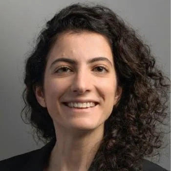 Smiling woman with curly hair against a neutral background, headshot style portrait.