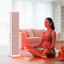Woman meditating at home with red light therapy panel for muscle recovery and skin health