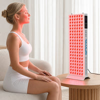 Woman seated facing the illuminated YA120-2W7 panel for an at-home face and upper-body red light therapy session